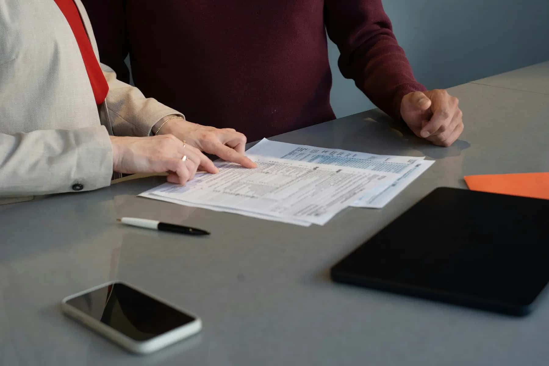 Two people reviewing printed documents at a table next to a tablet and a phone