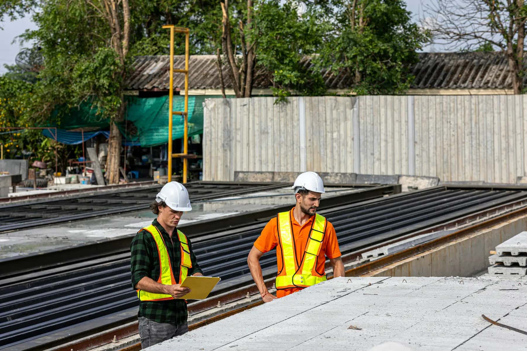 Two workers in hard hats and safety vests reviewing a clipboard at a job site