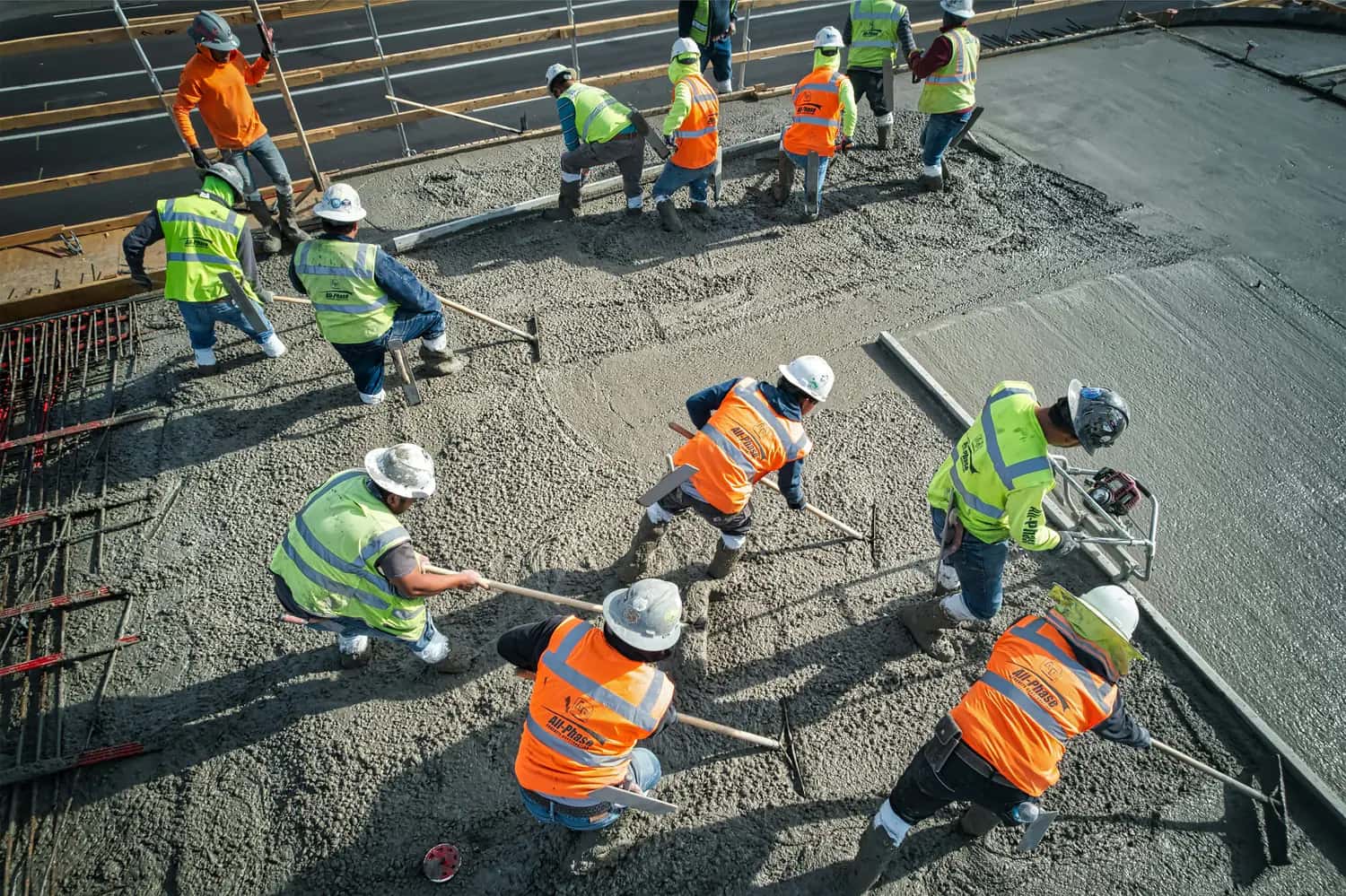 Overhead view of a construction crew in hard hats and hi-vis vests leveling fresh concrete