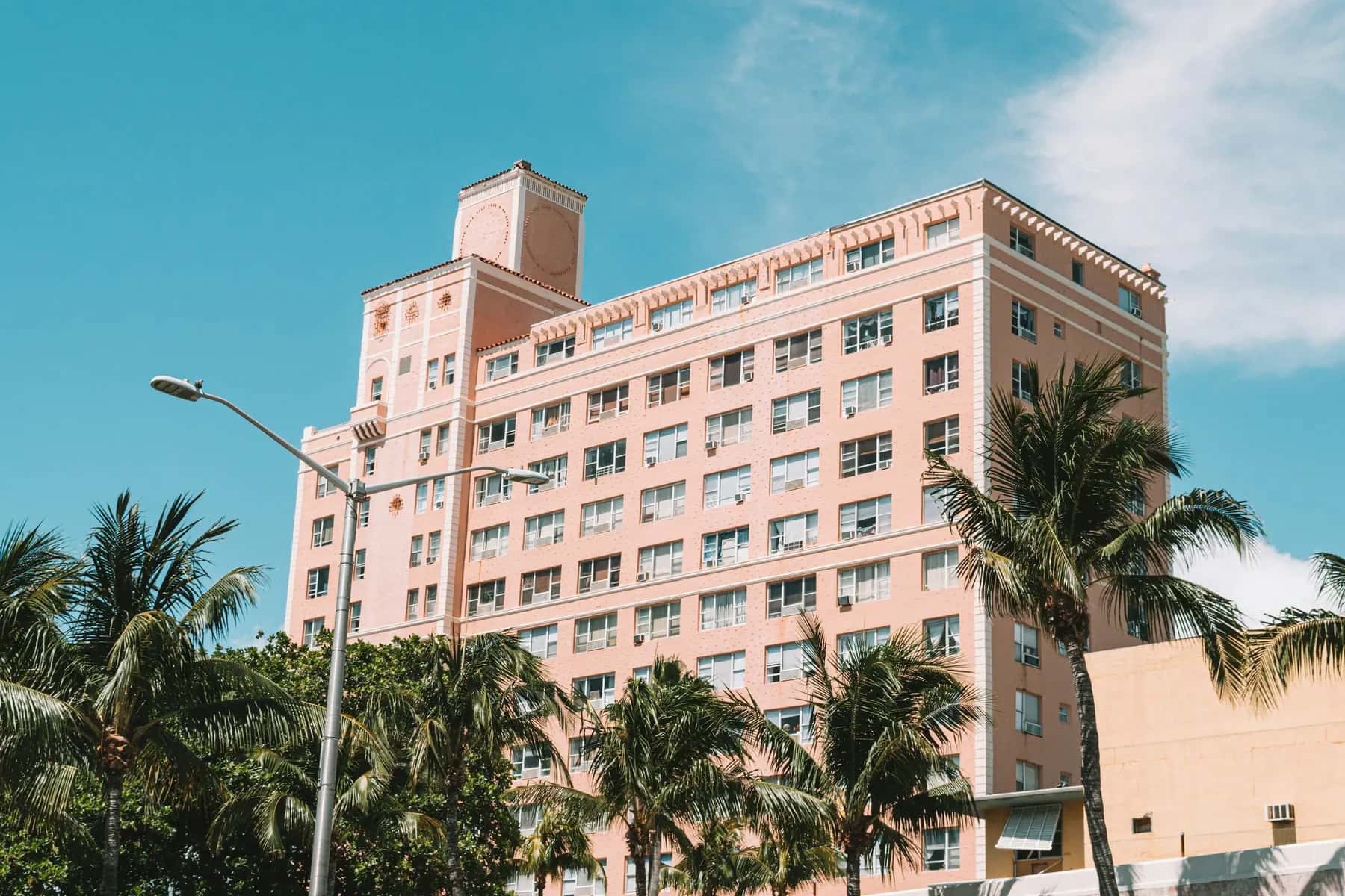 Pink mid-rise building framed by palm trees and a street light under a blue sky