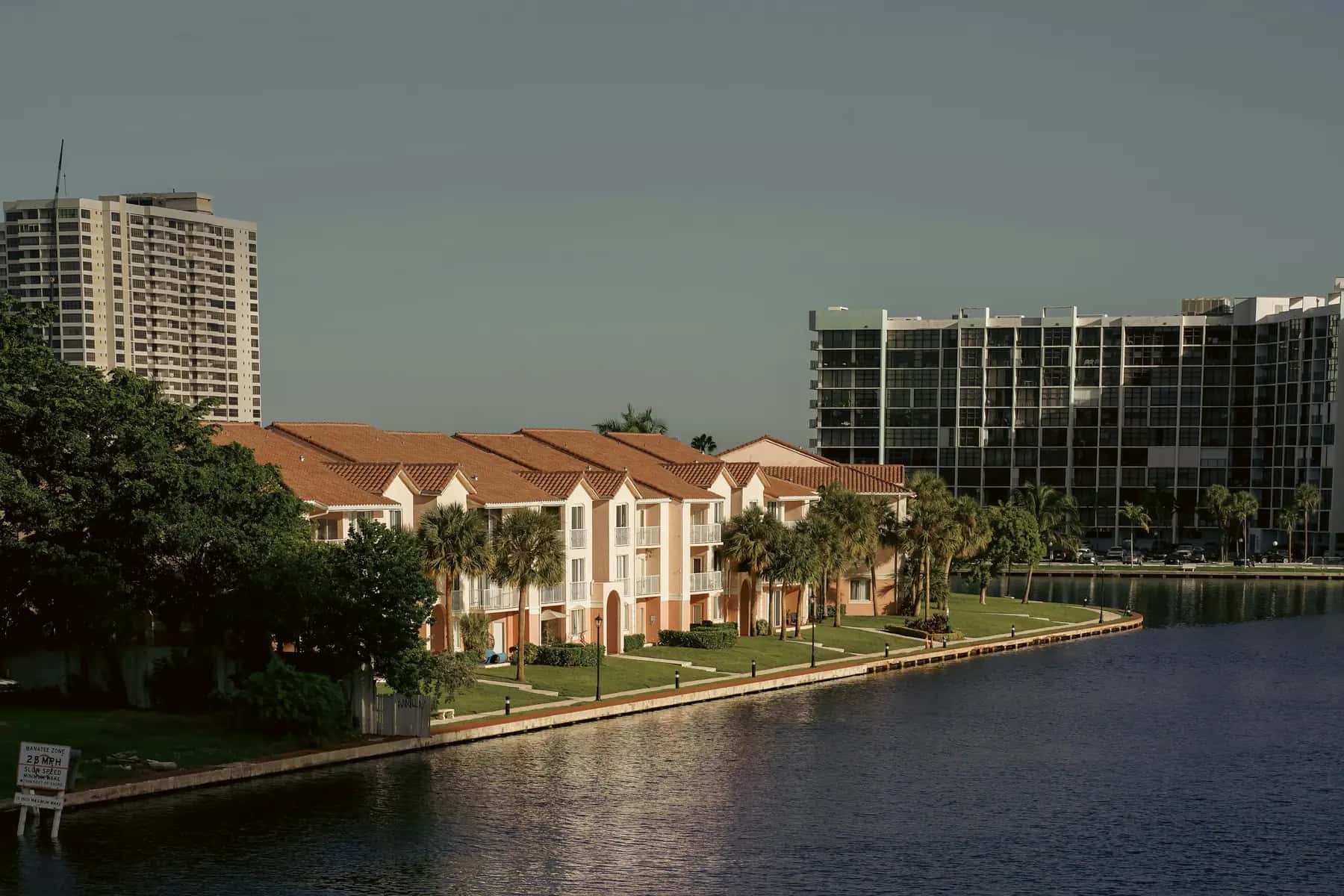 Waterfront condominium buildings with tile roofs, palms and a manicured lawn along a canal in South Florida