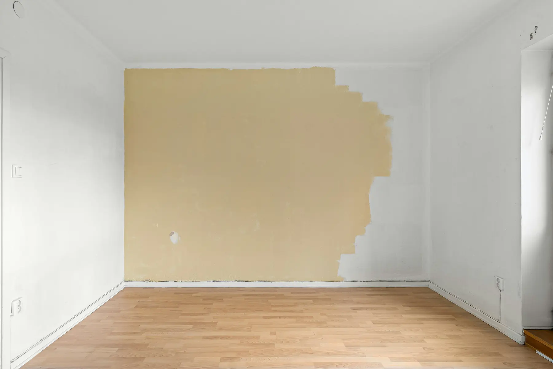 Empty apartment room with laminate floors and a wall partially painted during a make-ready