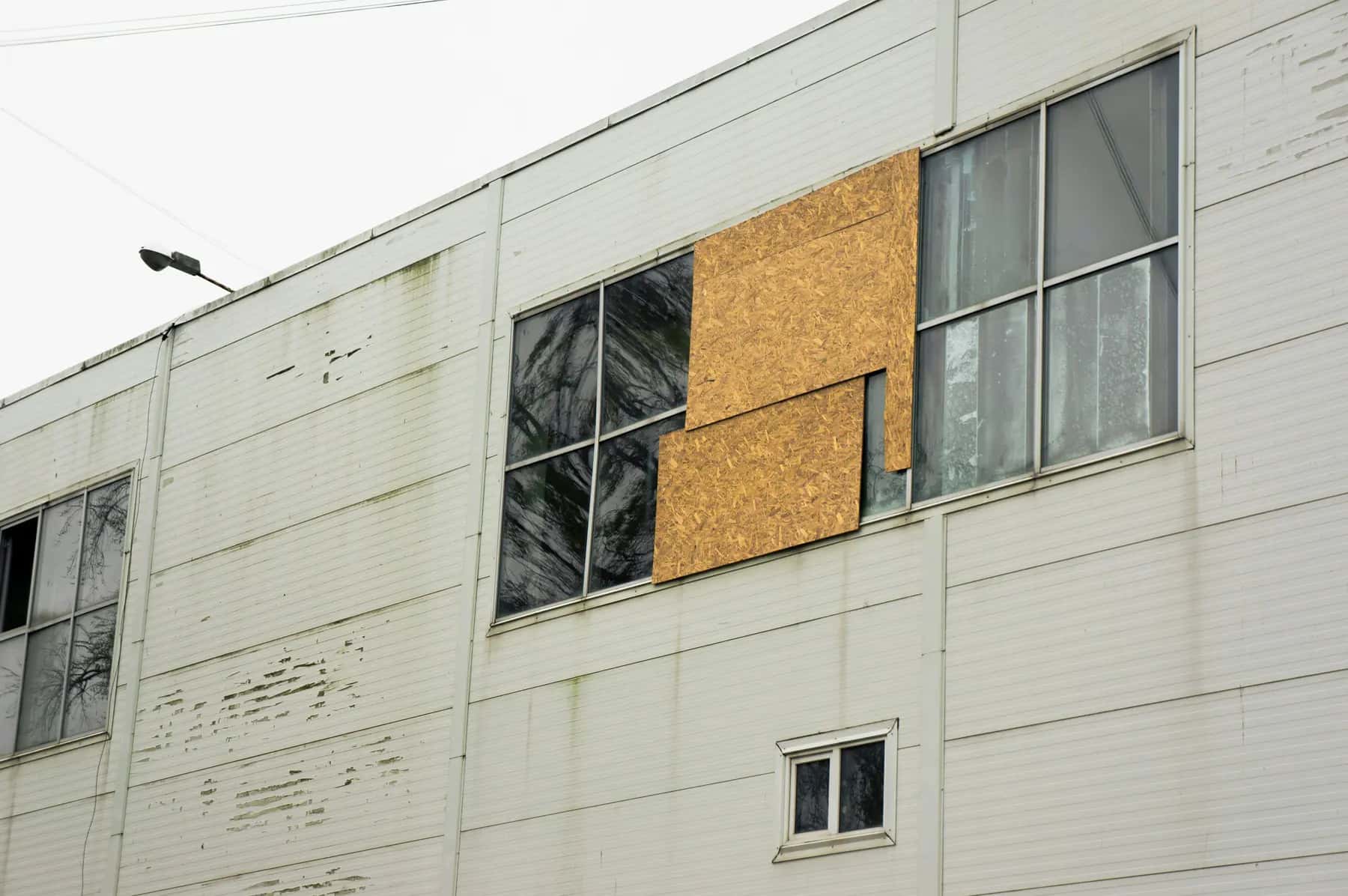 Plywood boards covering broken windows on a weathered commercial building