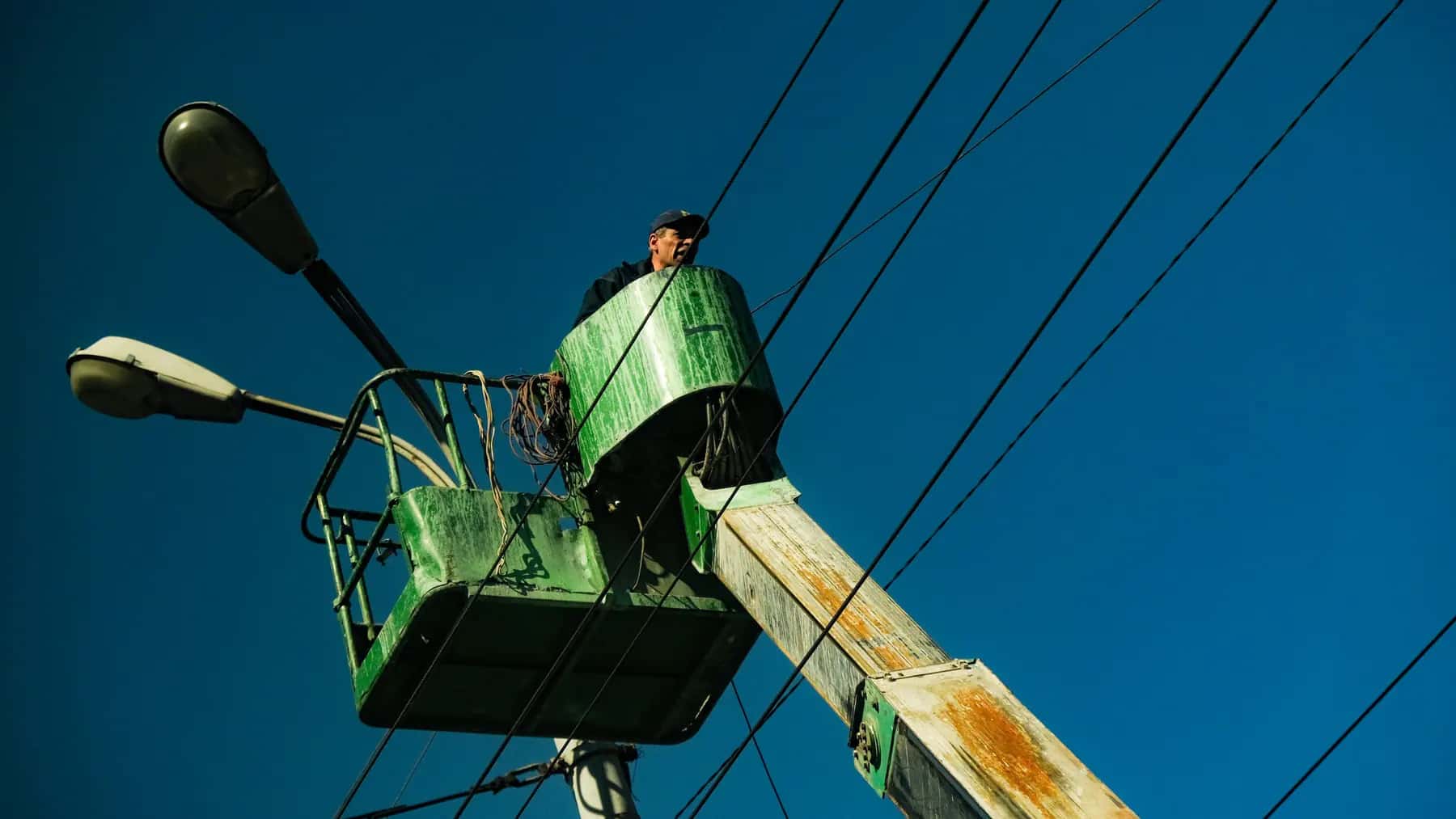 Utility worker in a bucket truck next to street light fixtures and overhead power lines