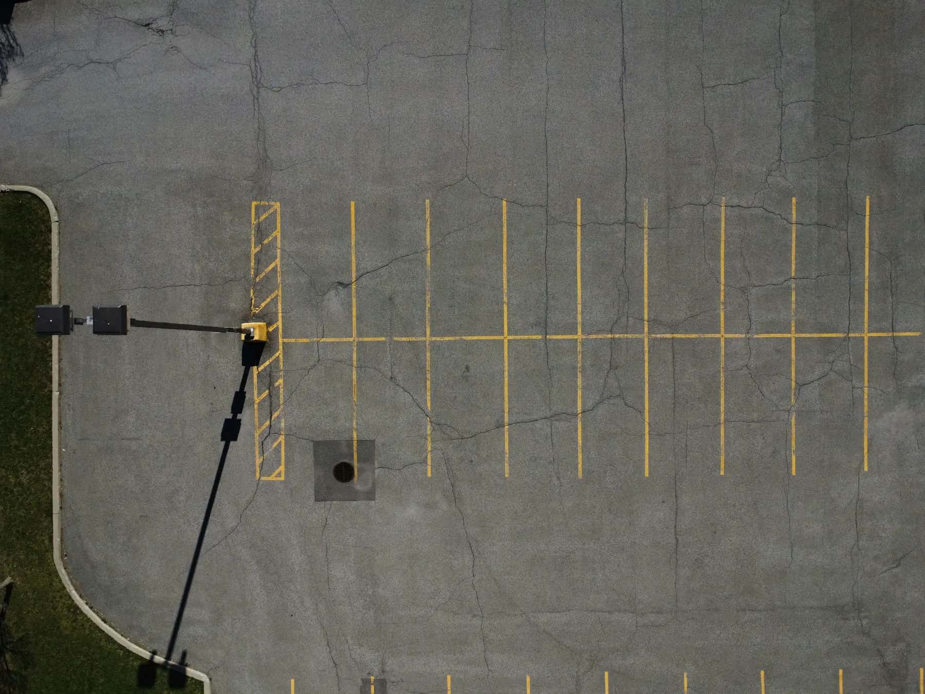 Overhead view of an asphalt parking lot with yellow striping and a light pole