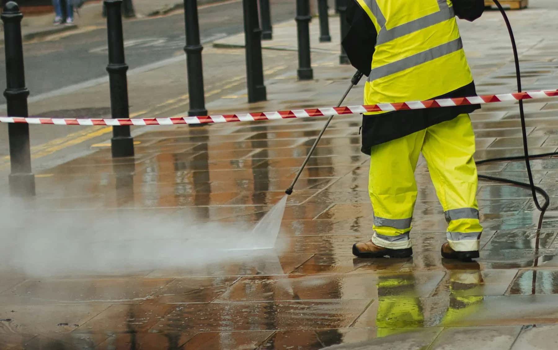 Worker in hi-vis gear pressure washing paving stones on a taped-off sidewalk