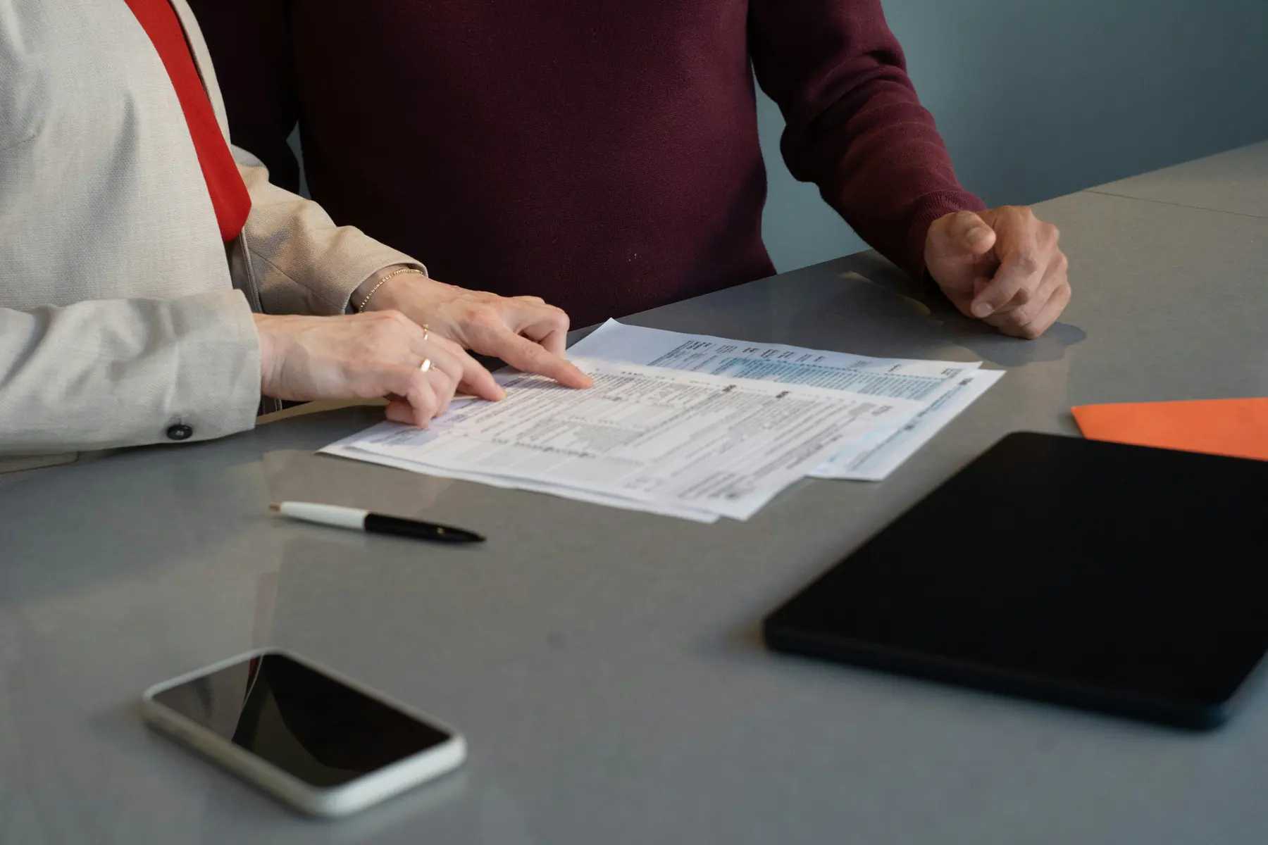 Two people reviewing printed documents at a table next to a tablet and a phone