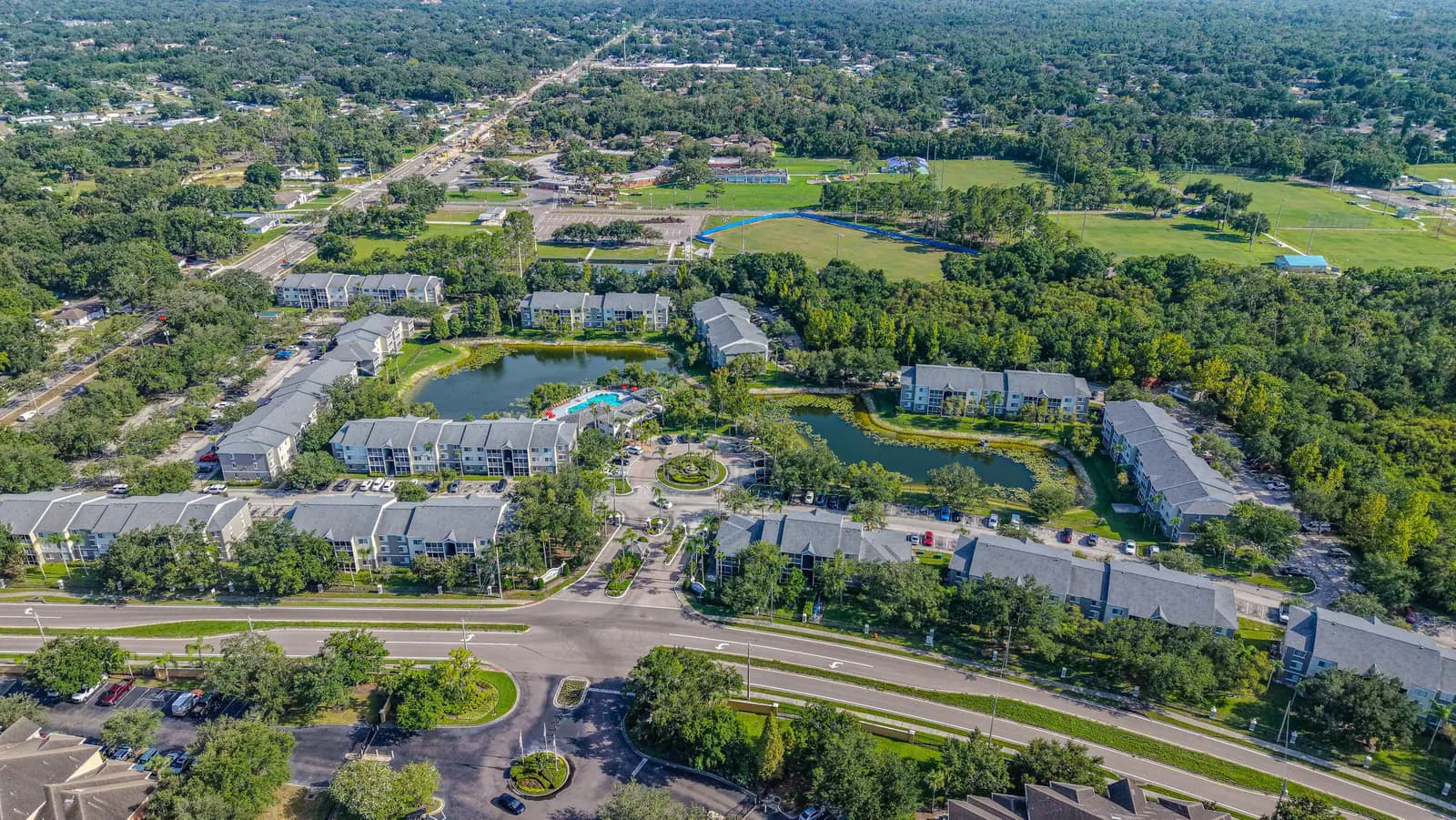 Aerial view of a garden-style apartment complex with retention ponds, a pool and surrounding tree canopy