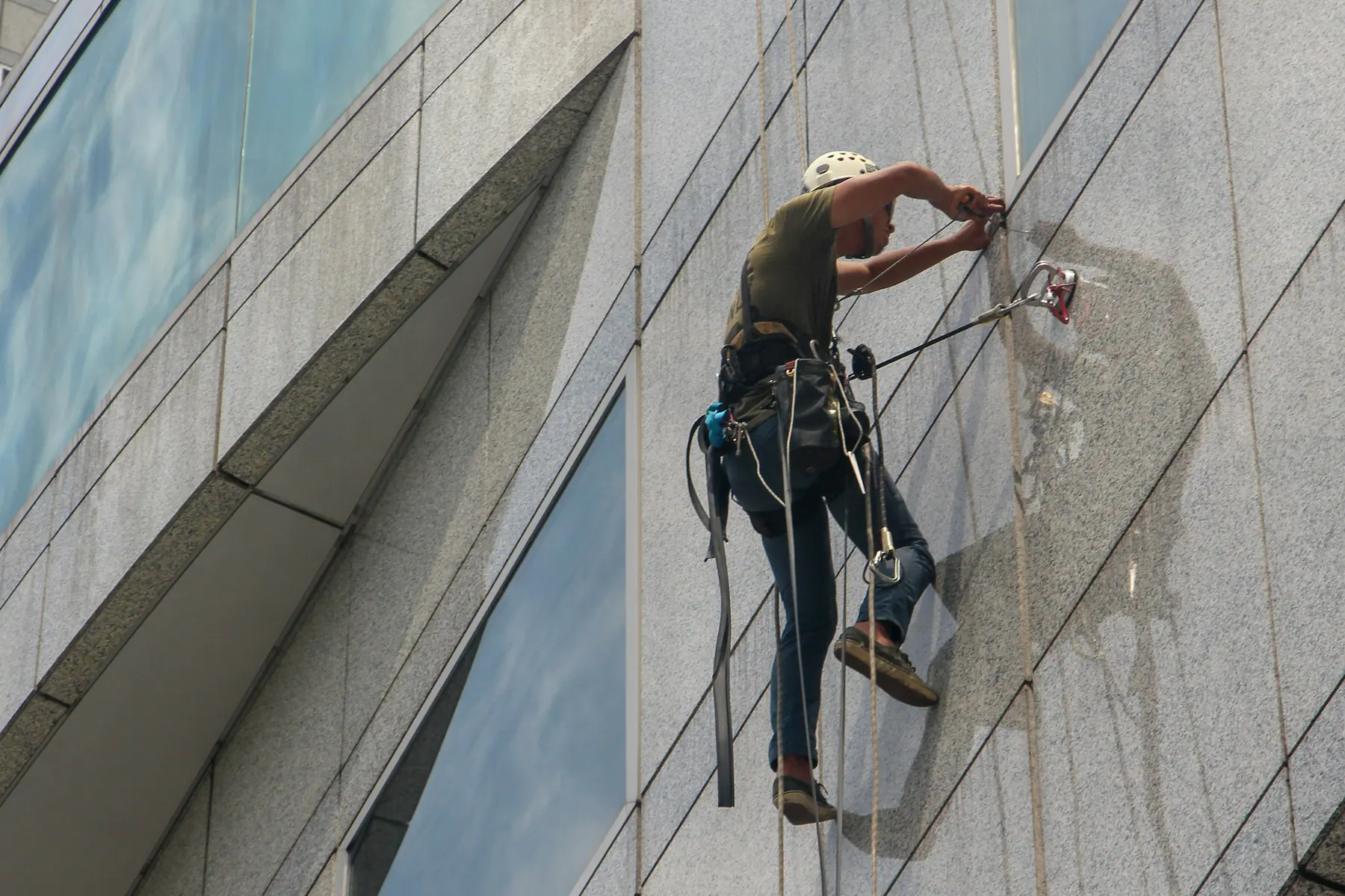 Rope-access worker cleaning the granite facade of a high-rise building