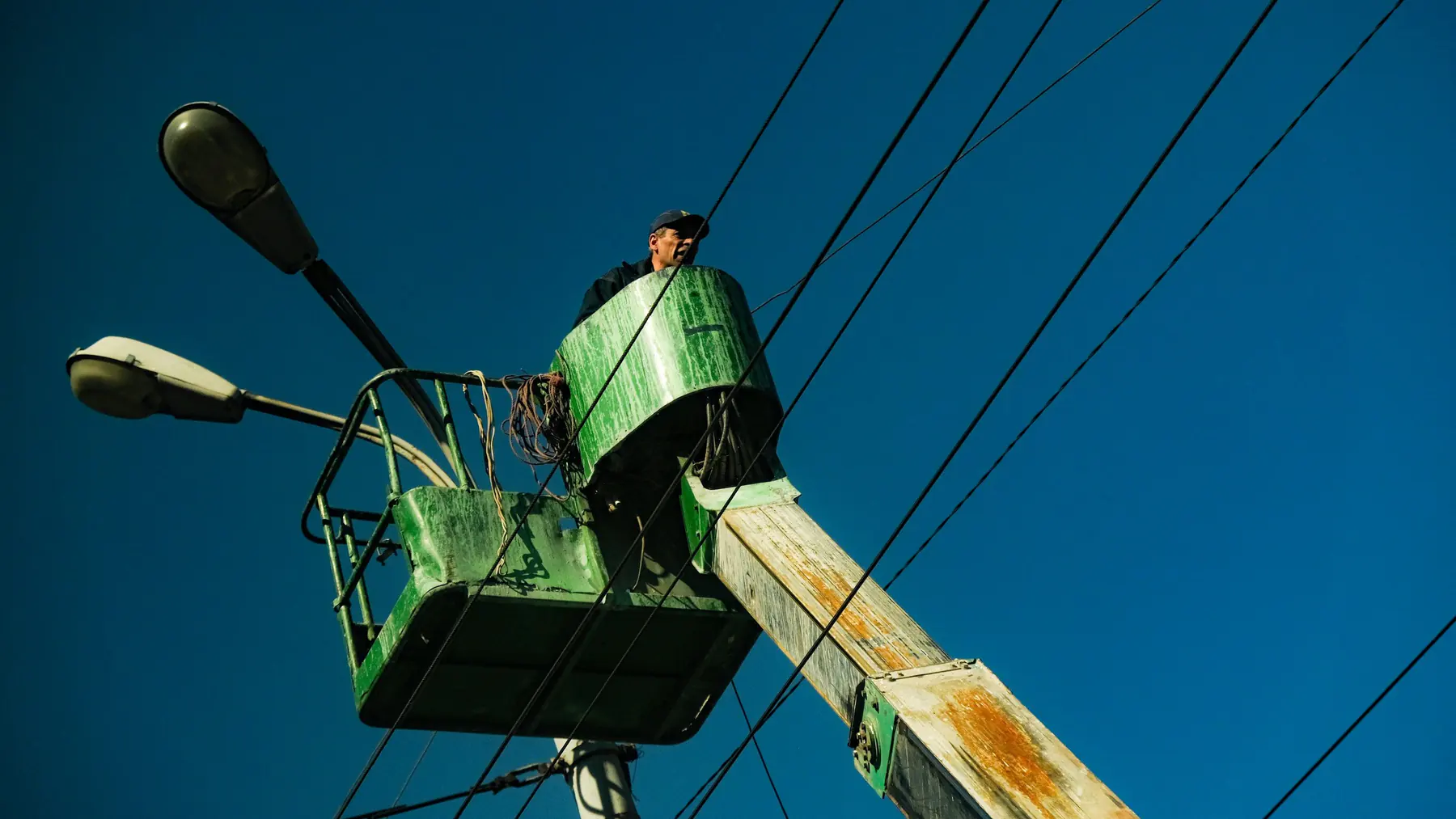 Utility worker in a bucket truck next to street light fixtures and overhead power lines