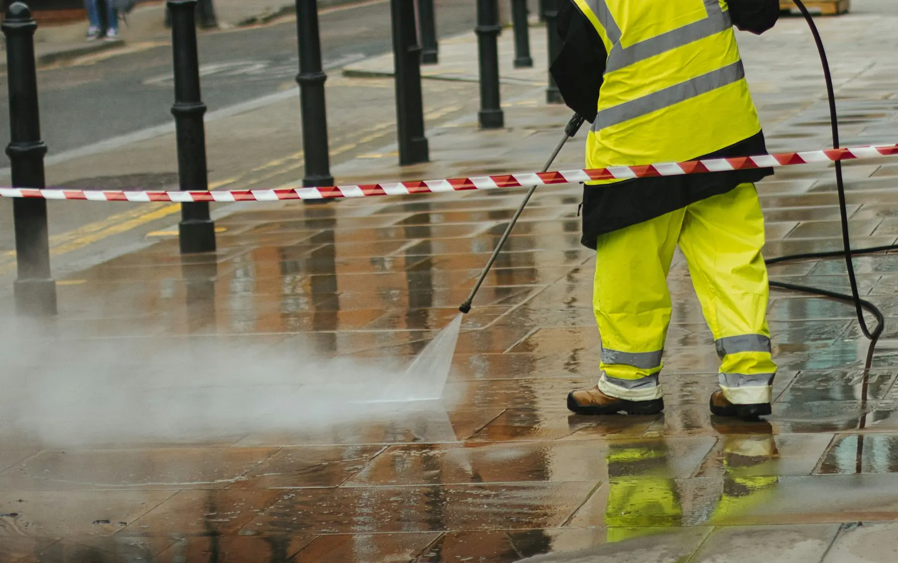 Worker in hi-vis gear pressure washing paving stones on a taped-off sidewalk