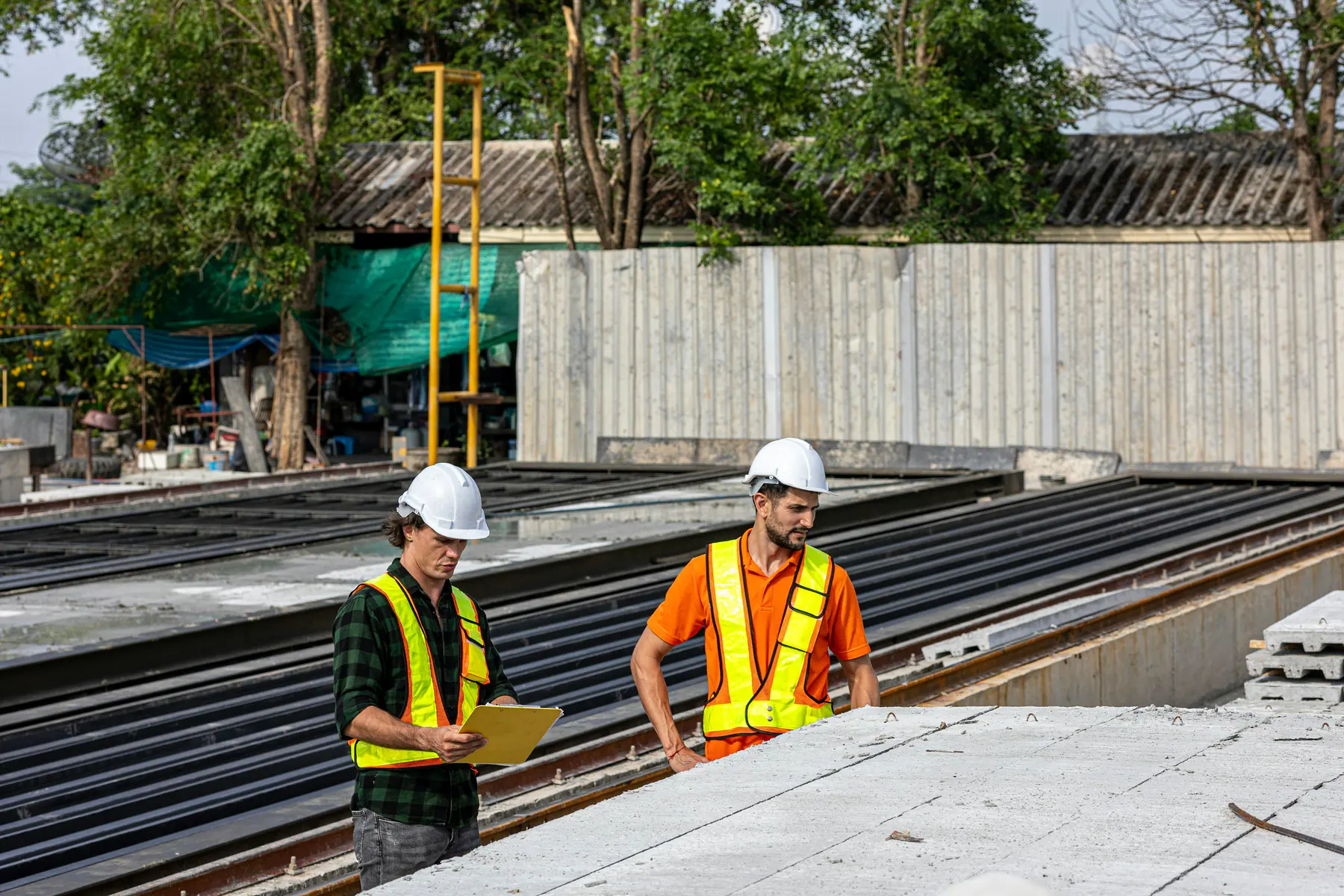Two workers in hard hats and safety vests reviewing a clipboard at a job site