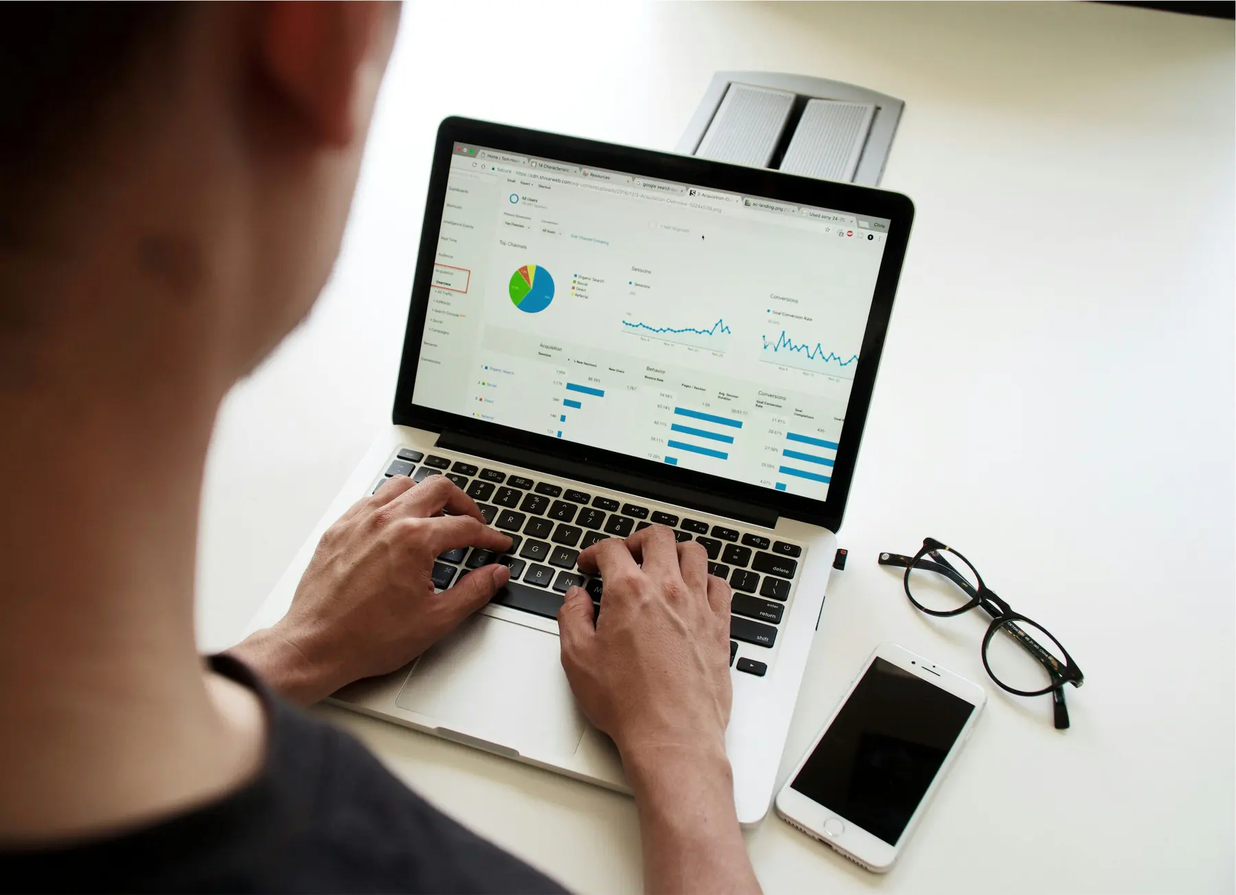 Person using a laptop showing charts and analytics dashboards on a white desk