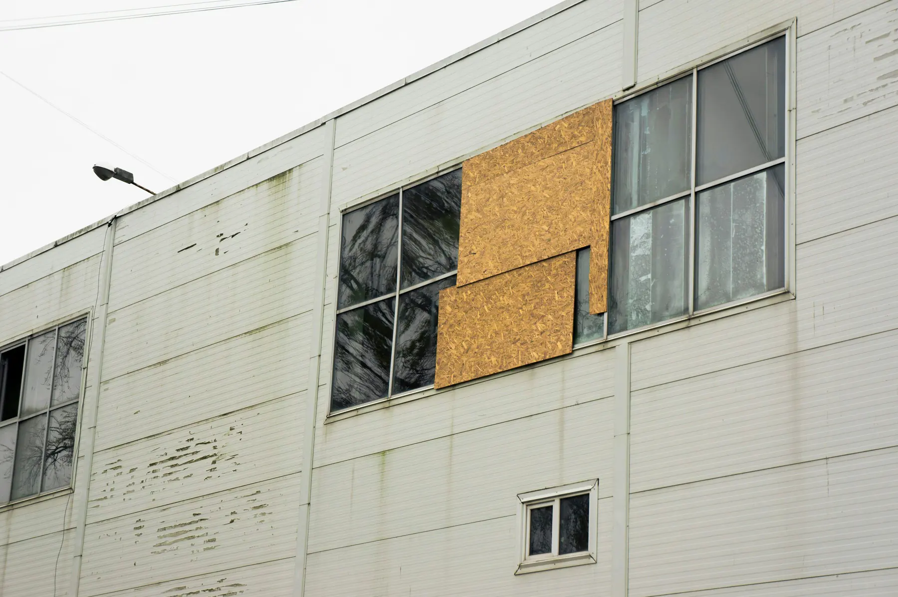 Plywood boards covering broken windows on a weathered commercial building