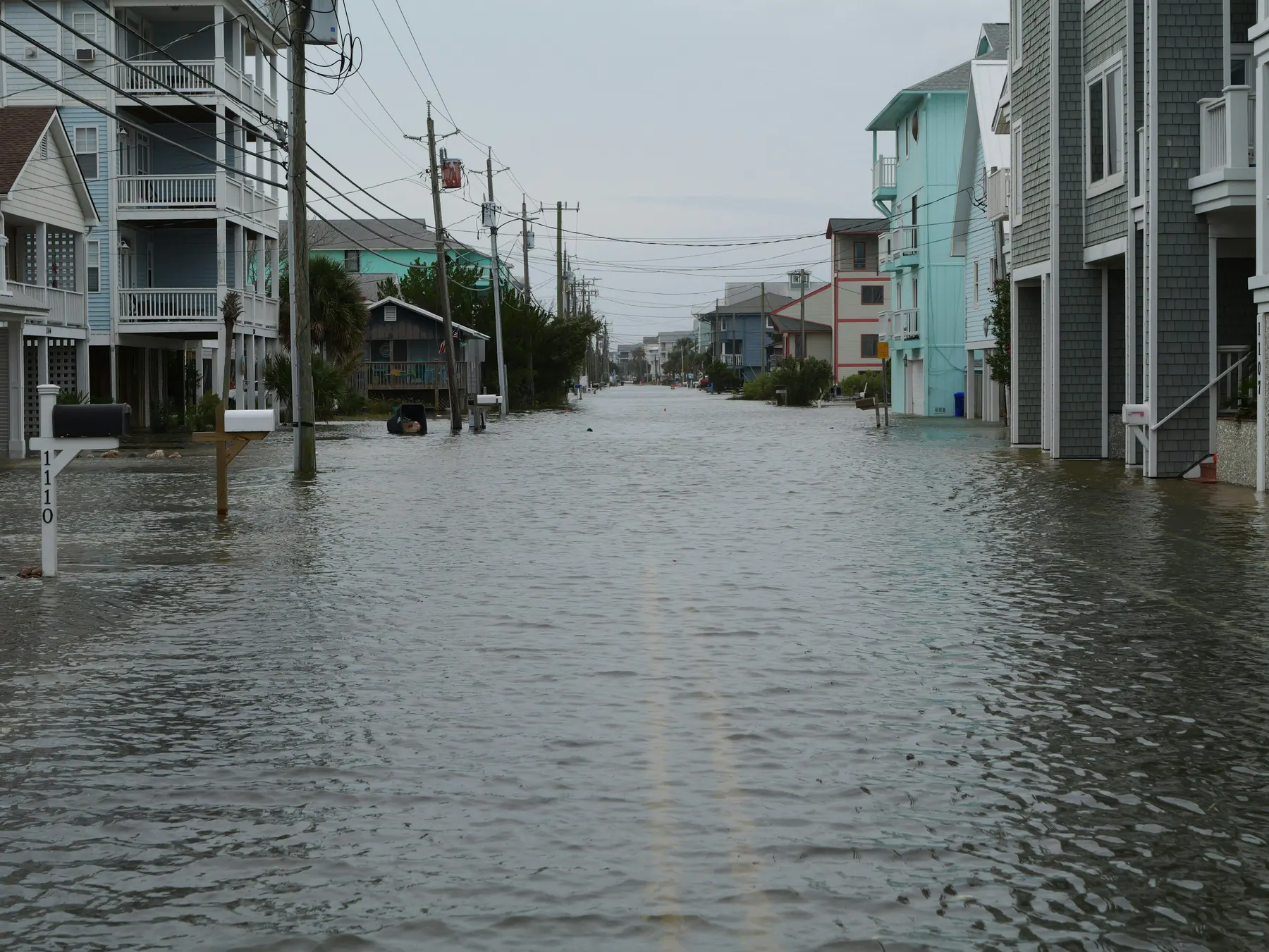 Flooded coastal street lined with raised homes and utility poles